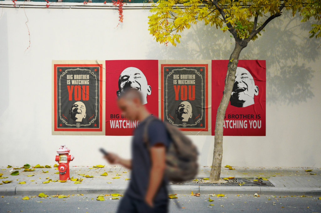 Man walks in front of propaganda posters that say "Big Brother Is Watching You" with Jeff Bezos's face