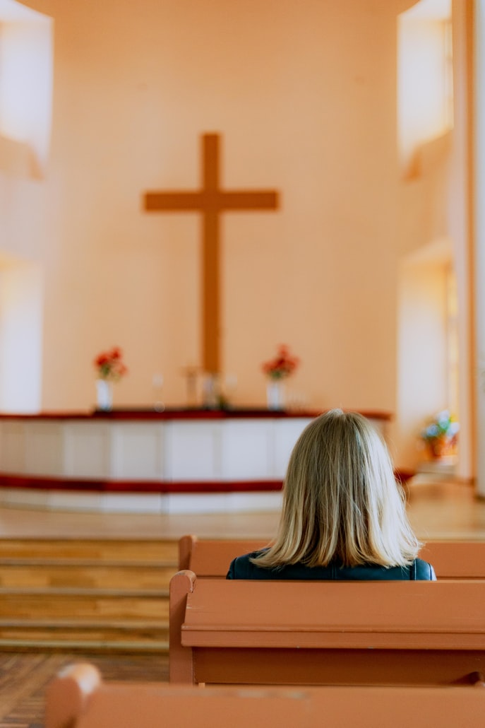 Blond woman sits in pew at church in front of cross