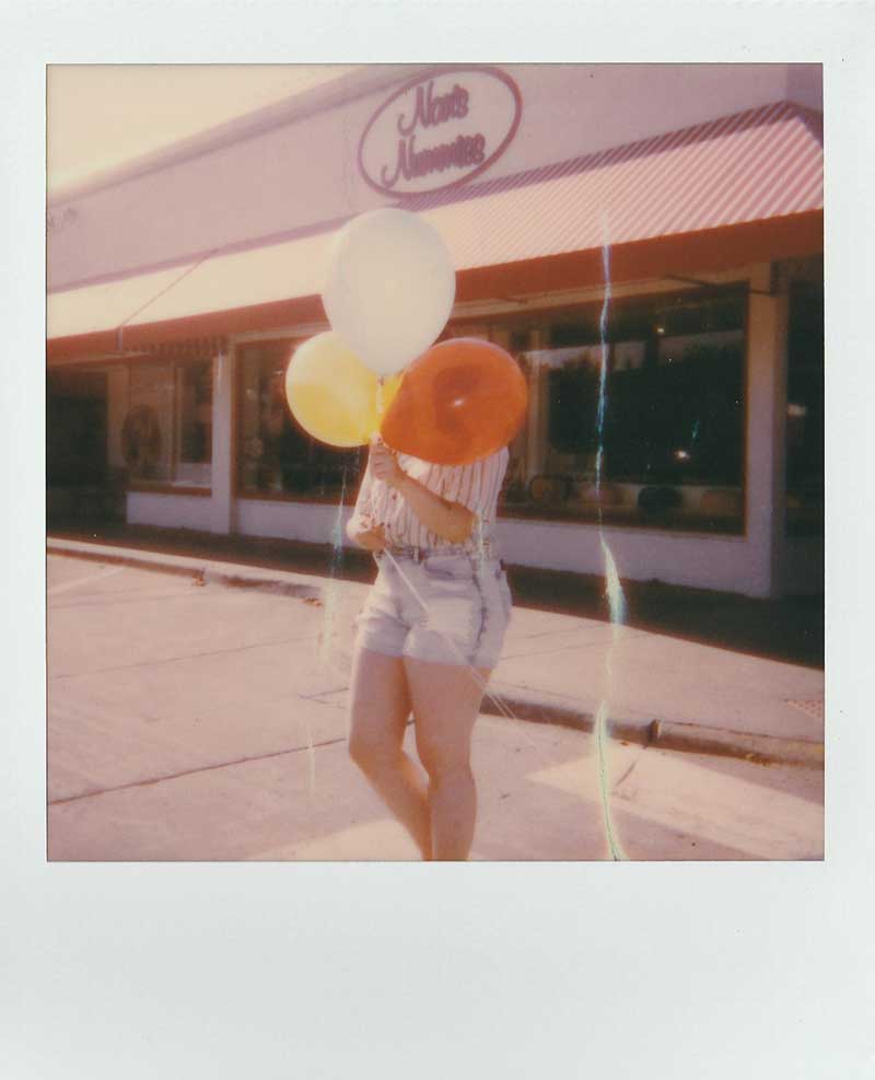 Fuzzy polaroid photo of a person with three balloons in front of a store - a brand is a memory