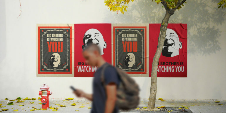 Man walks in front of propaganda posters that say "Big Brother Is Watching You" with Jeff Bezos's face